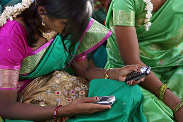 Young women look at their cellphone during a community meeting in India