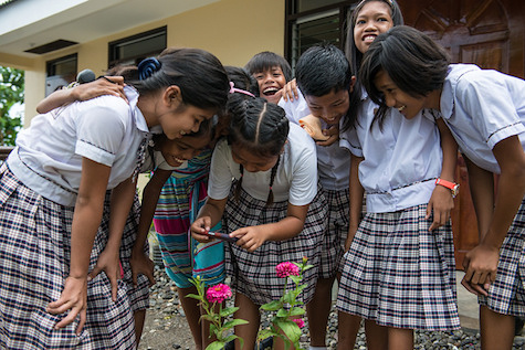 Girls in the Philippines look together at a mobile phone outside of a school.