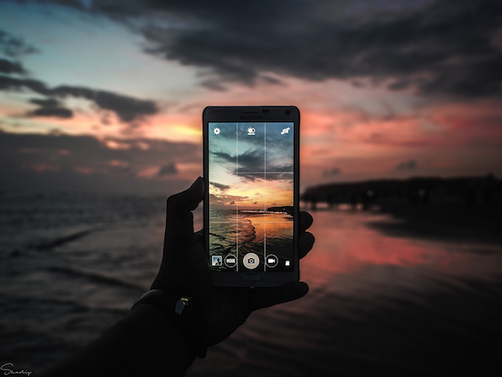 Hand holding a smartphone looking out onto a beach in Cox's Bazar, Bangladesh at sunset.
