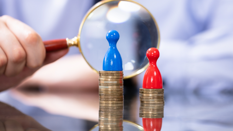 Man looking with magnifying glass at two coin stacks illustrating cost of gender gap