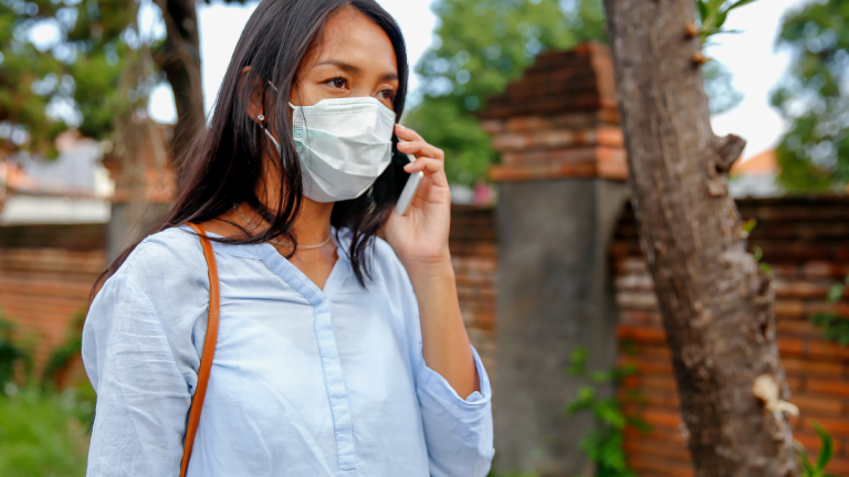 Portrait of Indonesian woman with face mask, calling on smartphone