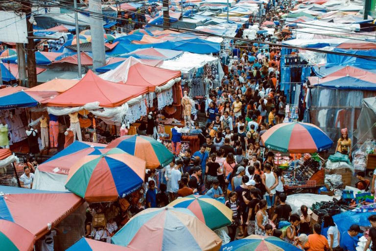 Scene of a crowded market with colorful stalls and umbrellas.